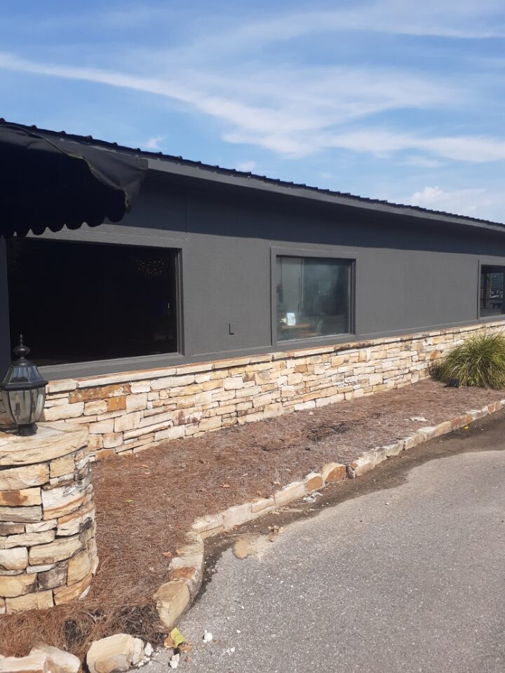 Long commercial building front finished in dark charcoal stucco above a stacked-stone base, with plate-glass windows and an awning